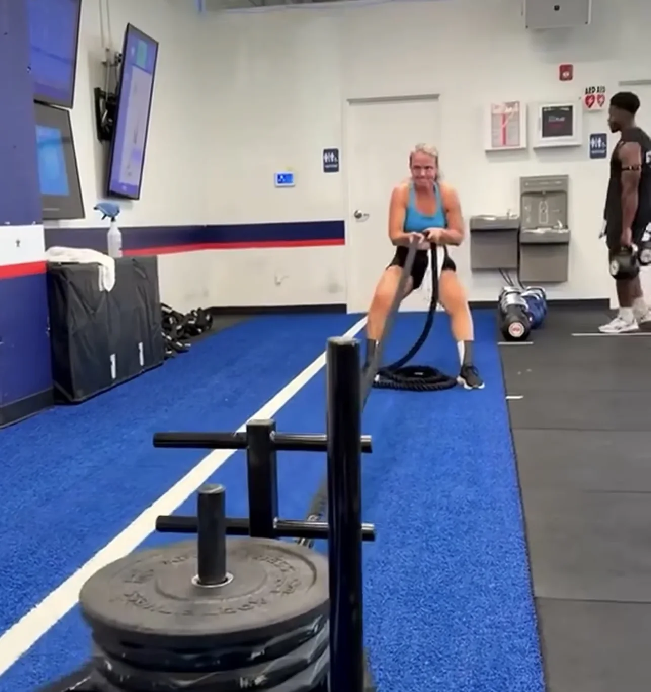 Jen Holley working battle ropes on blue turf in a gym