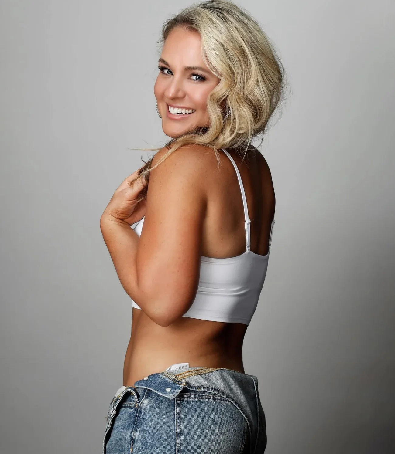 Jen Holley smiling over her shoulder in a white top and jeans